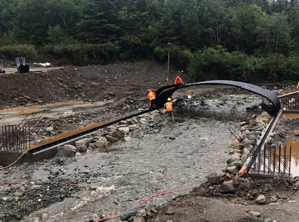 Wide view of crew assembling box culvert over stream