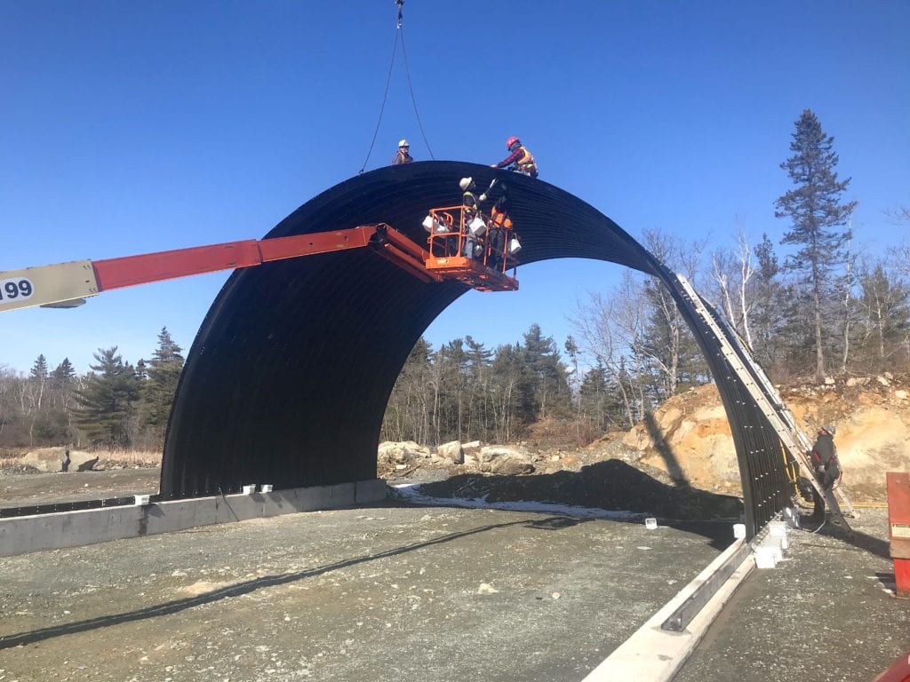 Crew assembling buried metal bridge with boom truck