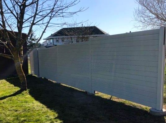 Close view of highway noise barrier wall by trees and houses