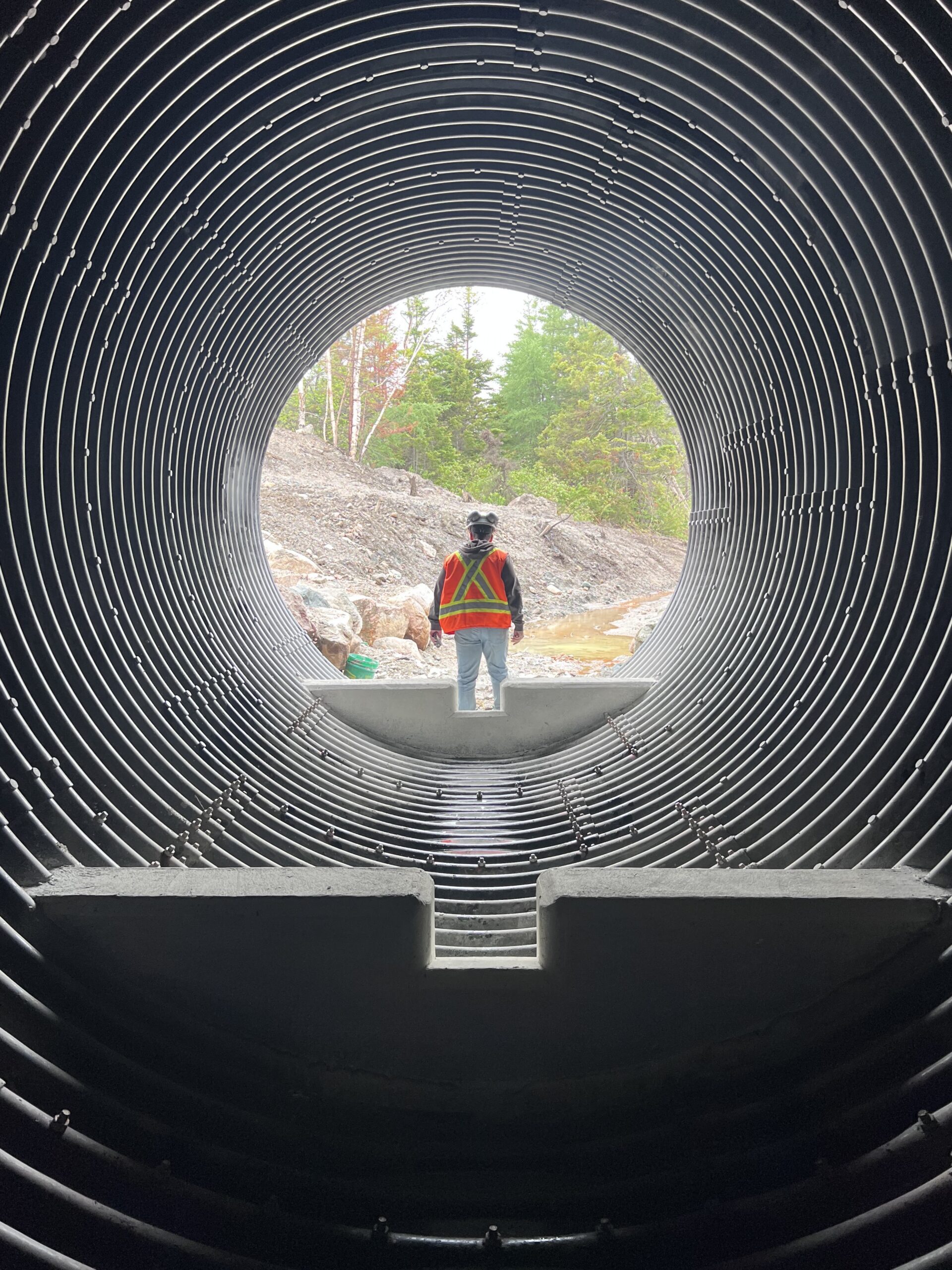 Front view of worker in safety vest standing near opening of AIL Bolt-A-Plate round culvert with fish baffle insert